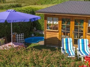 A wooden cabin with a pool, a covered patio with a table and chairs, and a blue umbrella. - Apartment A (2-3) - Apartments and Bed & Breakfast Eberle (Jungholz)