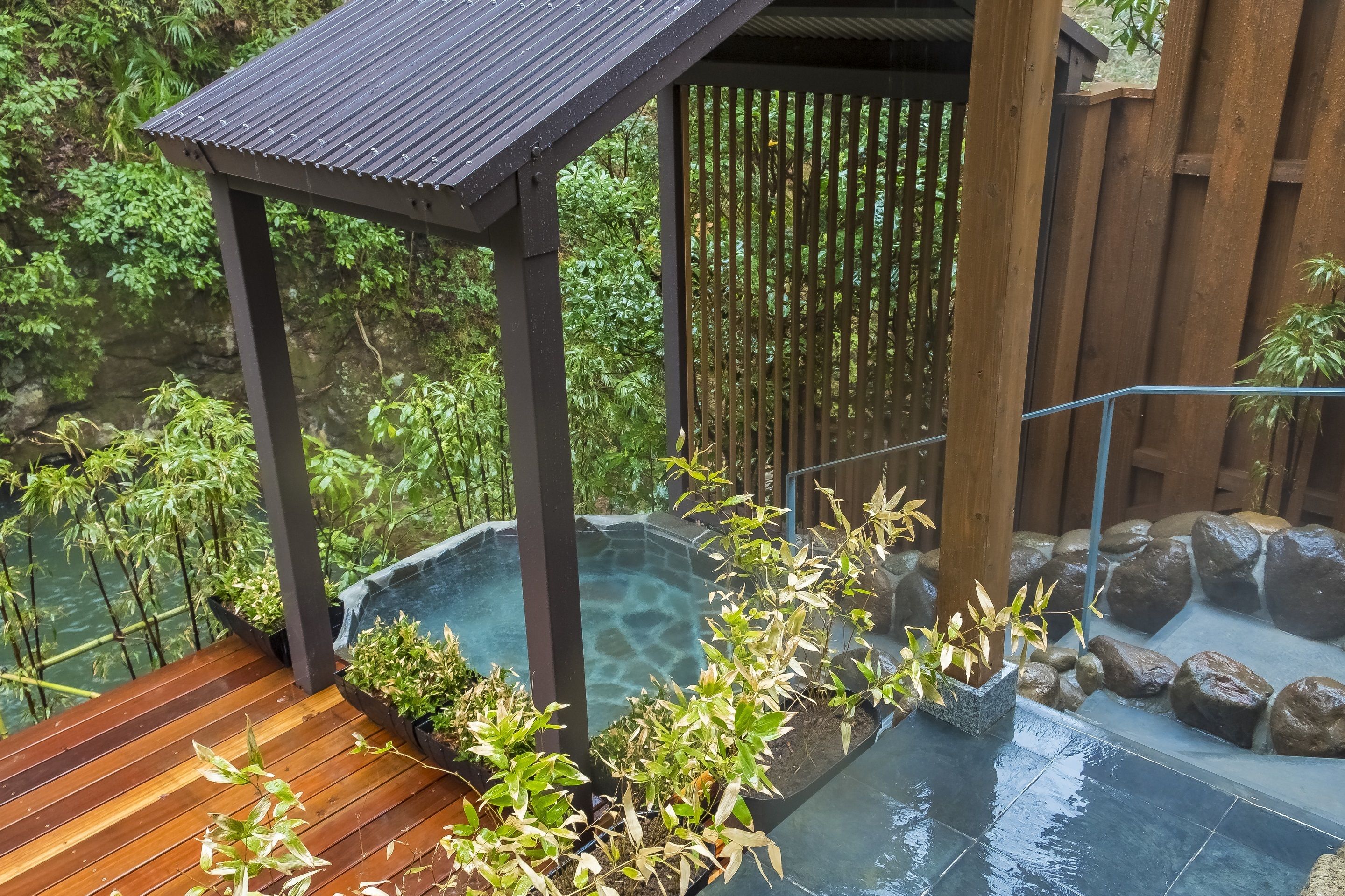 A wooden deck with a small covered area, a hot spring, and surrounding greenery.