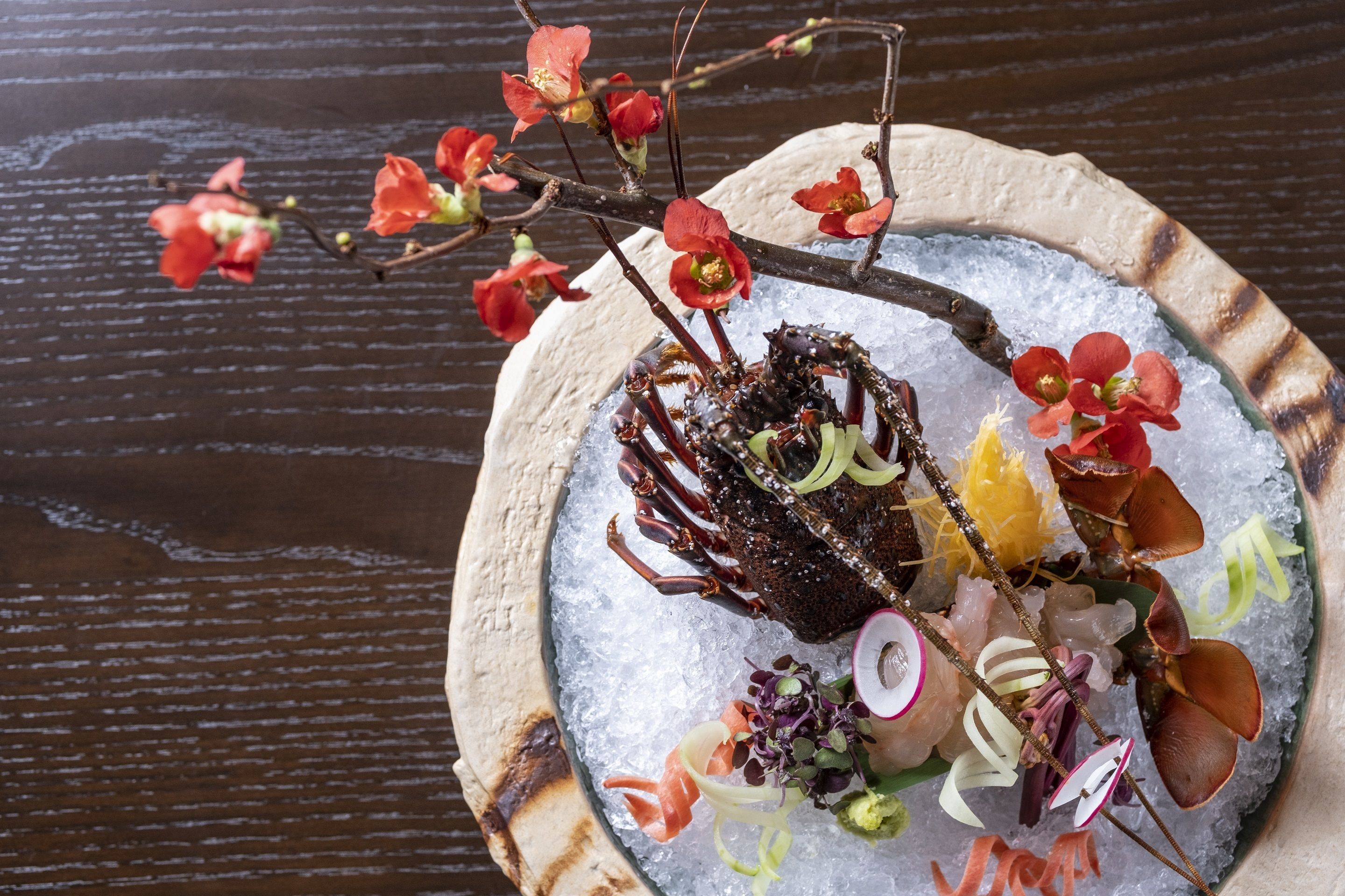 A seafood dish on a plate with ice, garnished with flowers and vegetables.