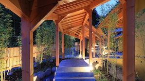A wooden covered walkway with steps leading to a building, surrounded by bamboo plants and rocks.