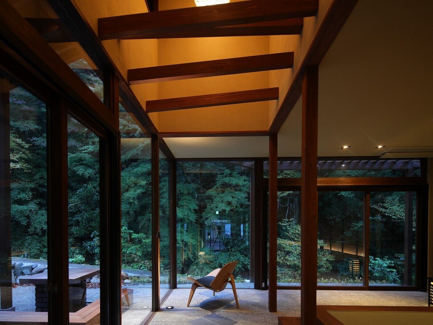 Un intérieur moderne avec de grandes fenêtres en verre, des poutres en bois et un coin salon offrant une vue sur une forêt.