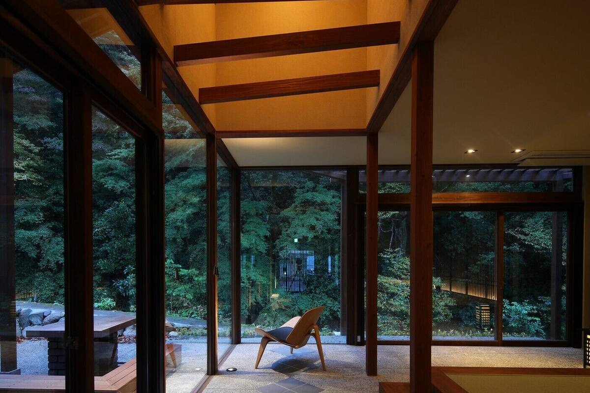 Un interior moderno con amplios ventanales, vigas de madera y una zona de estar con vistas a un bosque.