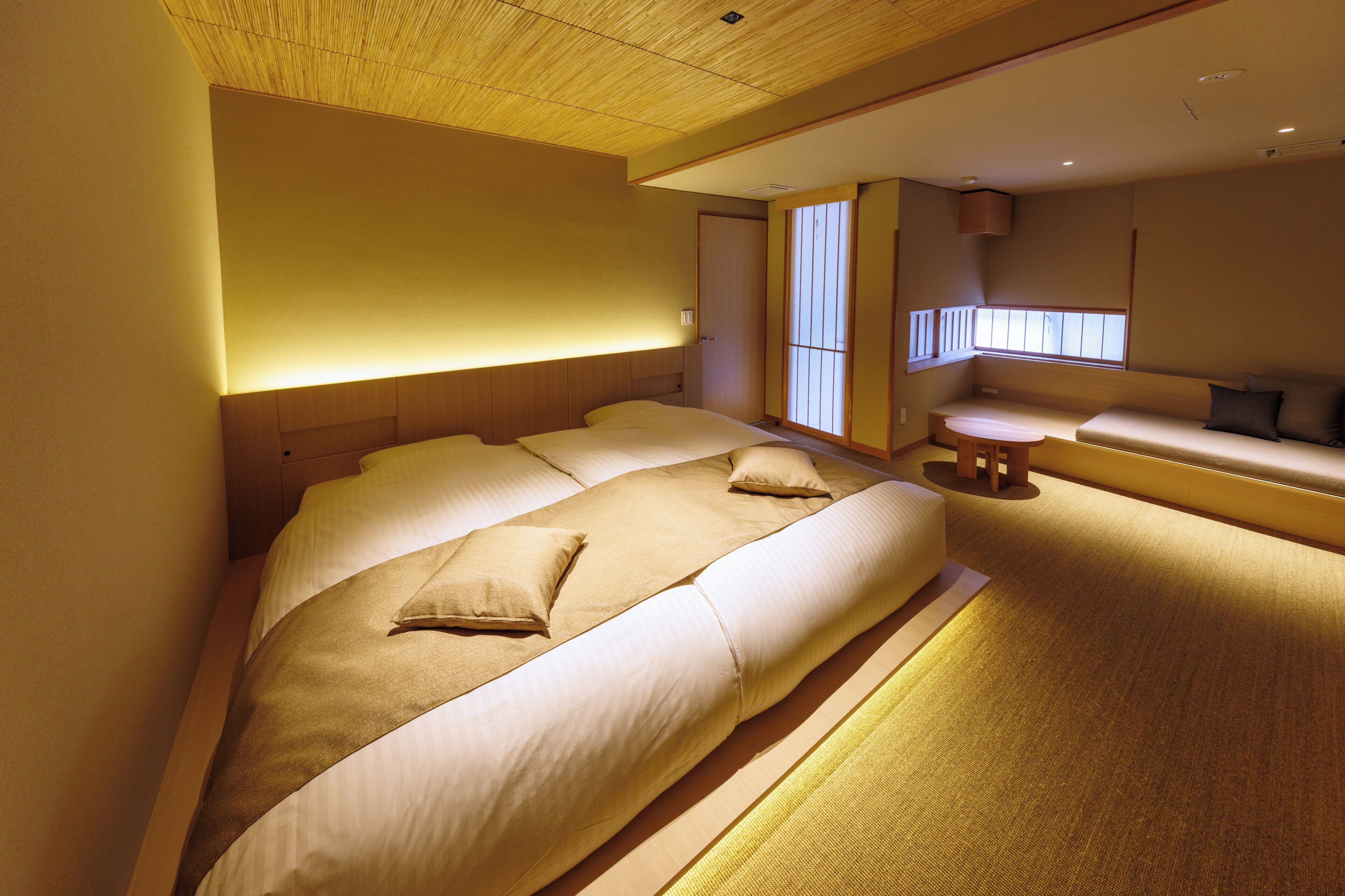 A hotel room with a large bed, a small seating area, and a window with blinds.