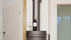 Ein moderner Holzofen mit Glasscheibe, eine Weinflasche und zwei Gläser darauf.