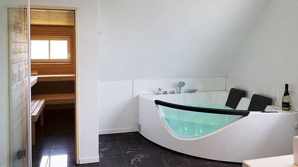 Ein modernes Badezimmer mit einer freistehenden Badewanne, einer Holzbank und einer Weinflasche am Rand.
