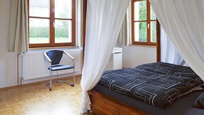 Ein Schlafzimmer mit einem Bett, einem Sessel und zwei Fenstern mit Vorhängen.