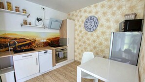 Una cuina moderna amb armaris blancs, forn integrat, microones i zona de menjador amb taula i cadires blanques.