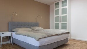 Et soveværelse med en grå seng, et hvidt natbord og en hvid garderobe med glasdøre.