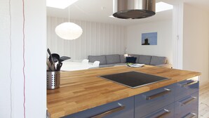 Et moderne køkken med træbordplade, indbyggede hårde hvidevarer og en grå sofa i baggrunden.