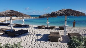 A beach with thatched umbrellas, lounge chairs, and a clear view of the ocean.