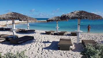 A beach with thatched umbrellas, lounge chairs, and a clear view of the ocean.