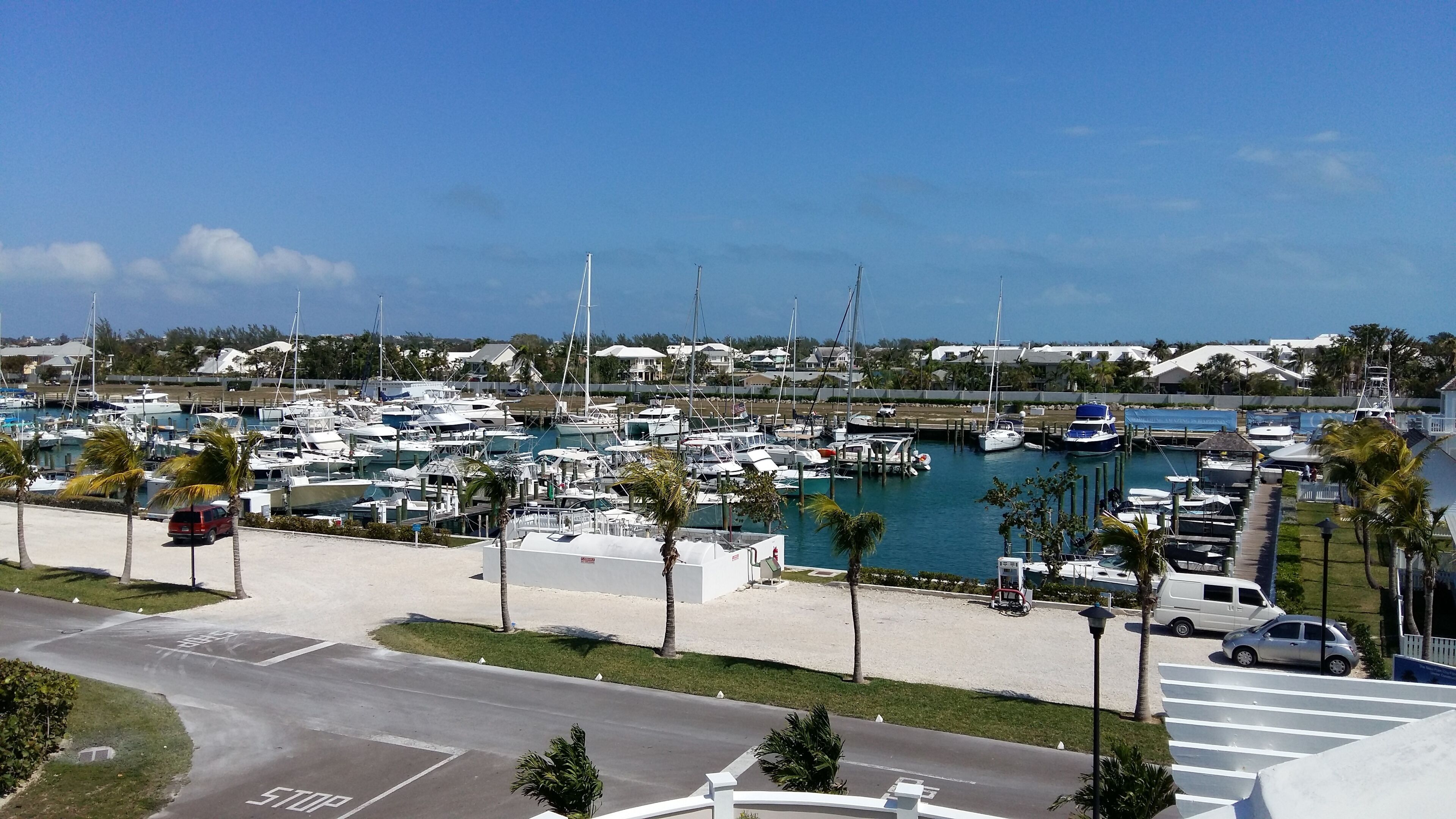 A marina with multiple boats docked, a parking area with a stop sign, and a clear view of the marina in the background.