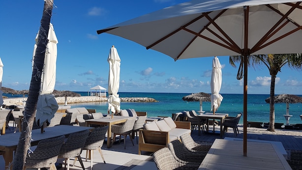A beachside lounge with wicker furniture, white umbrellas, and a view of the ocean.