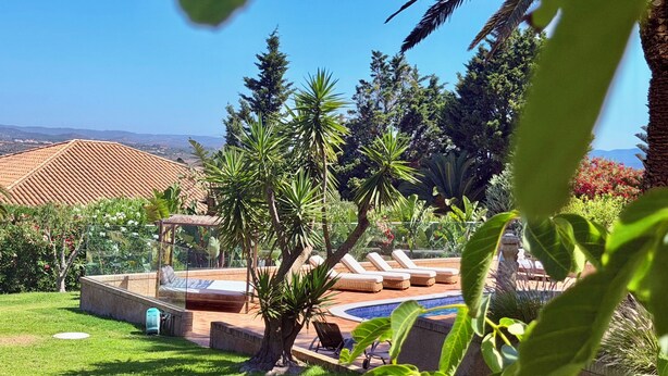 A pool area with lounge chairs, surrounded by greenery and a clear view of distant hills. - Villa with pool and view in Luz/Lagos (Luz)