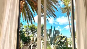 A view through a window with curtains, featuring a garden with palm trees and a stone structure. - Villa with pool and view in Luz/Lagos (Luz)