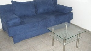Un sofá azul con una mesita de centro de vidrio en una habitación con suelo de baldosas.