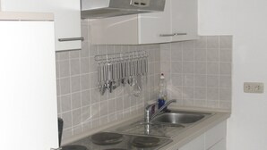 Una cocina con estufa, lavamanos y utensilios colgando.