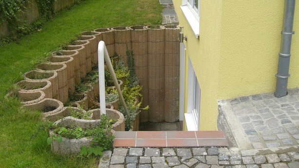 Un jardín con un muro de ladrillo y una tubería blanca.