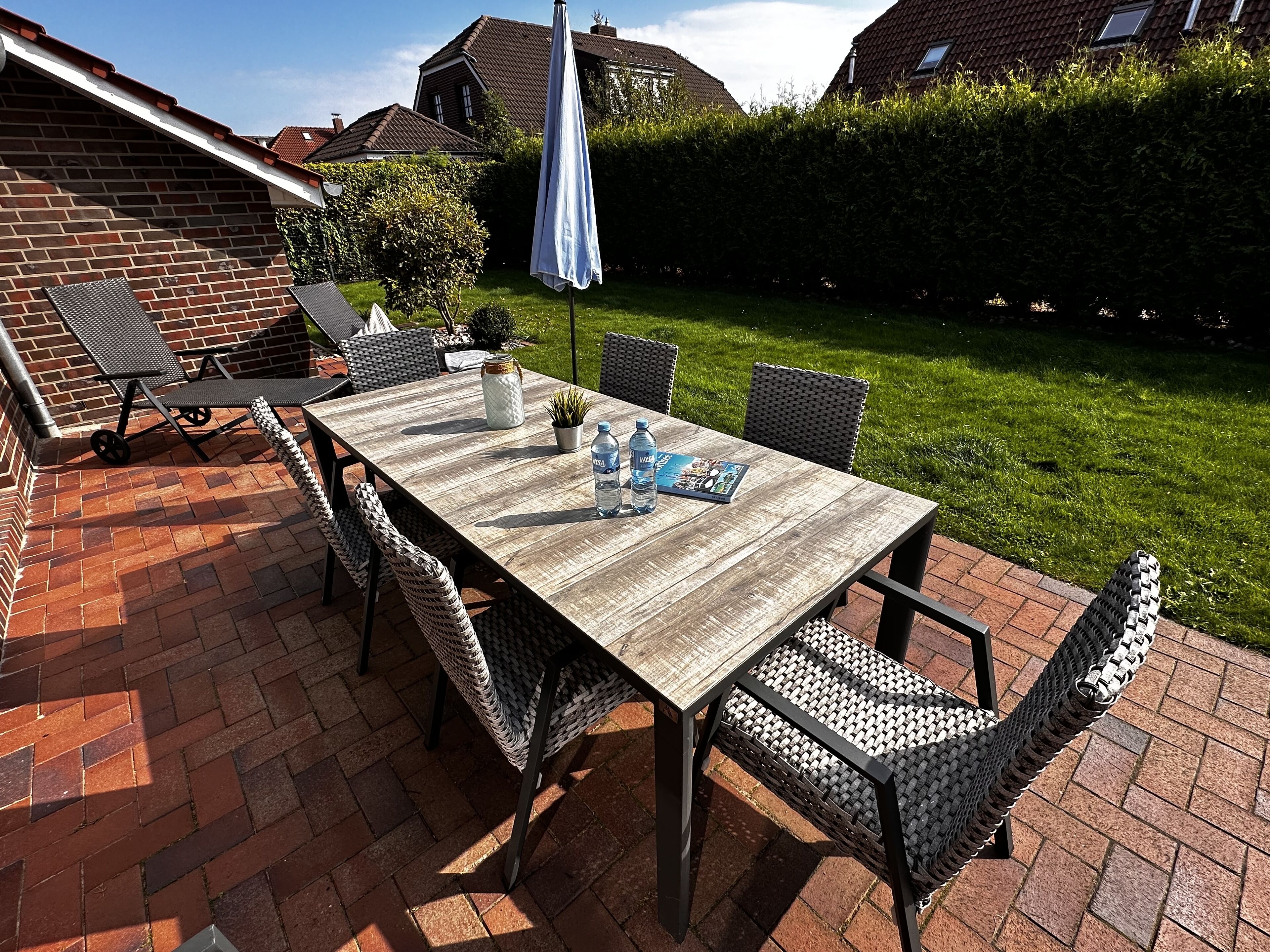 Une terrasse avec une table en bois, des chaises en osier et une bouteille d’eau.