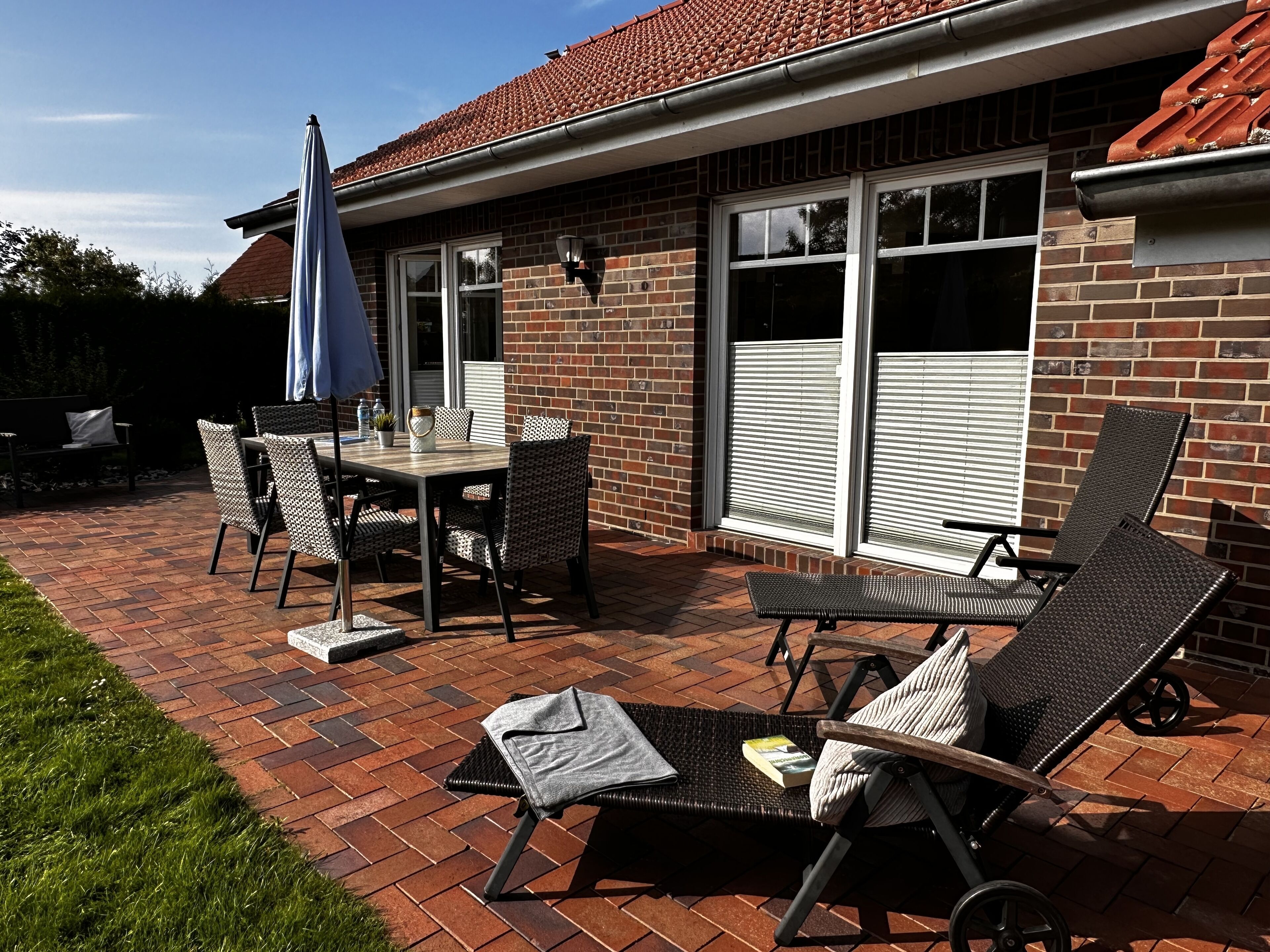 Une terrasse avec un sol en briques, une table entourée de chaises et un parasol.
