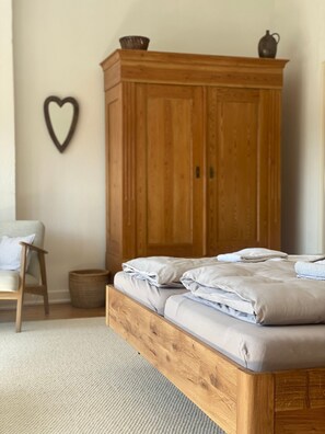 A bedroom with a wooden bed frame, a chair, a basket, and a wooden wardrobe.