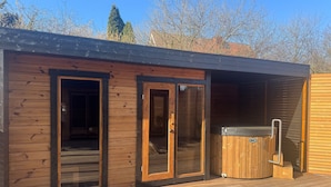 Una cabaña de madera con puertas correderas de vidrio, un jacuzzi y una terraza.