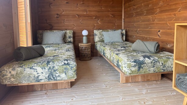 Una cabaña de madera con dos literas, un taburete tejido y una lámpara colgante.