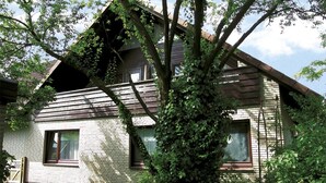 Una casa de dos pisos con techo inclinado, paredes de ladrillo y ventanas grandes.