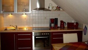 Una cocina compacta con estufa, horno y lavamanos. Hay armarios sobre la encimera y una ventana con persianas.