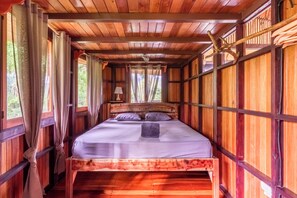 Ein Schlafzimmer in einer Holzhütte mit Bett, Vorhängen und einem Fenster.