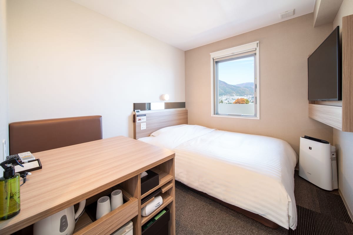 A hotel room with a bed, a desk, a chair, a TV, and a window with a view of mountains.