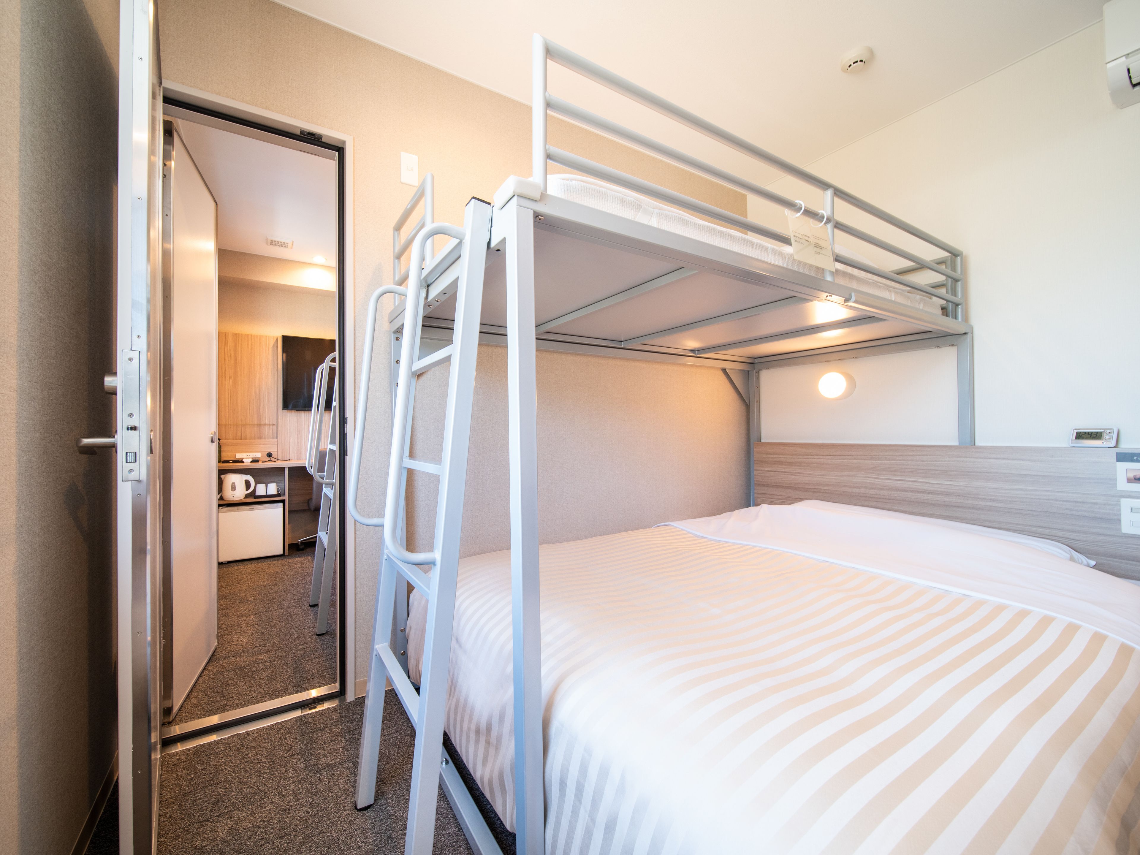A bunk bed with a ladder, a bedside table, and a wall-mounted clock.