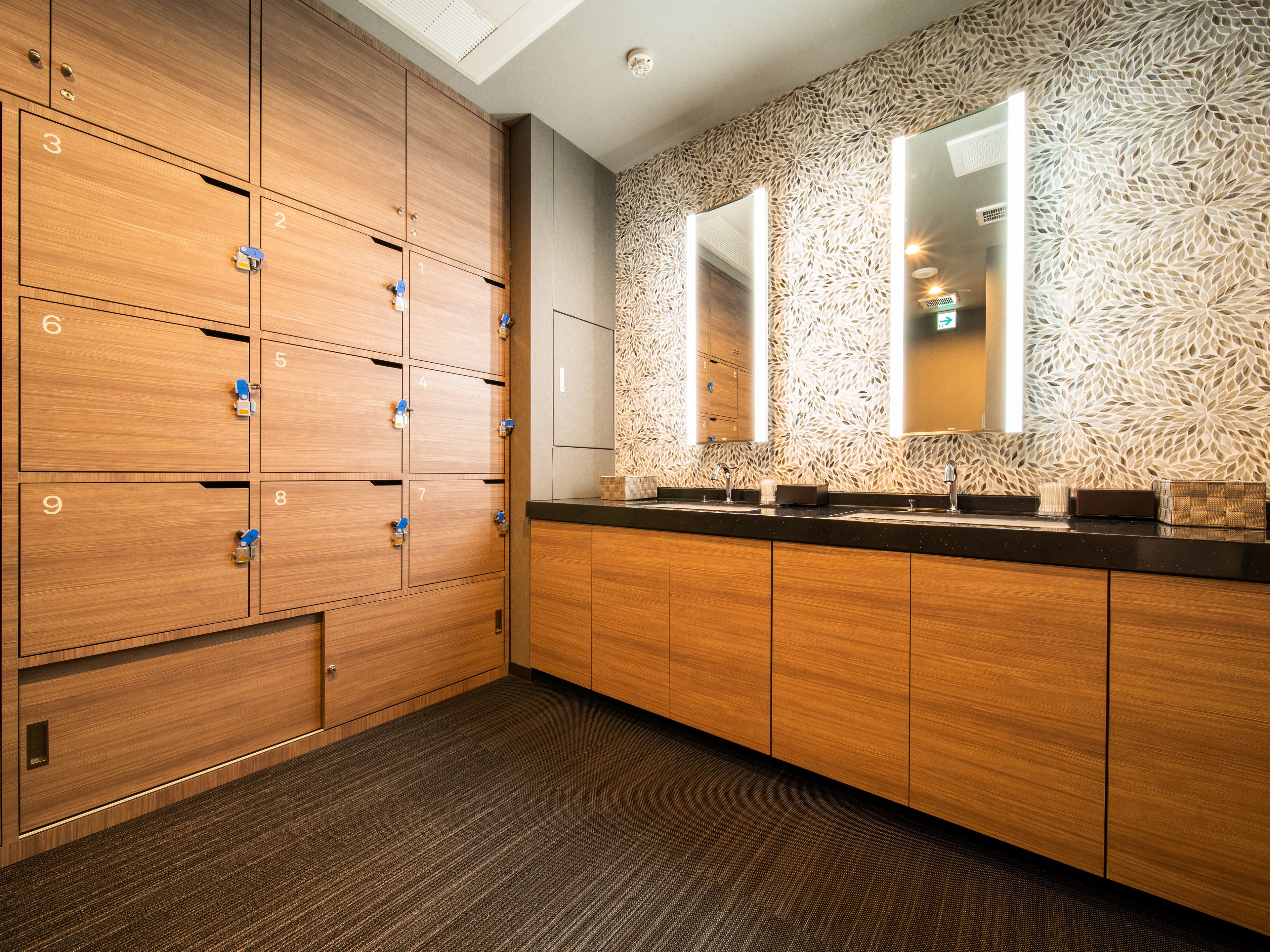 A modern bathroom with wooden lockers, a patterned wall, and a large mirror.