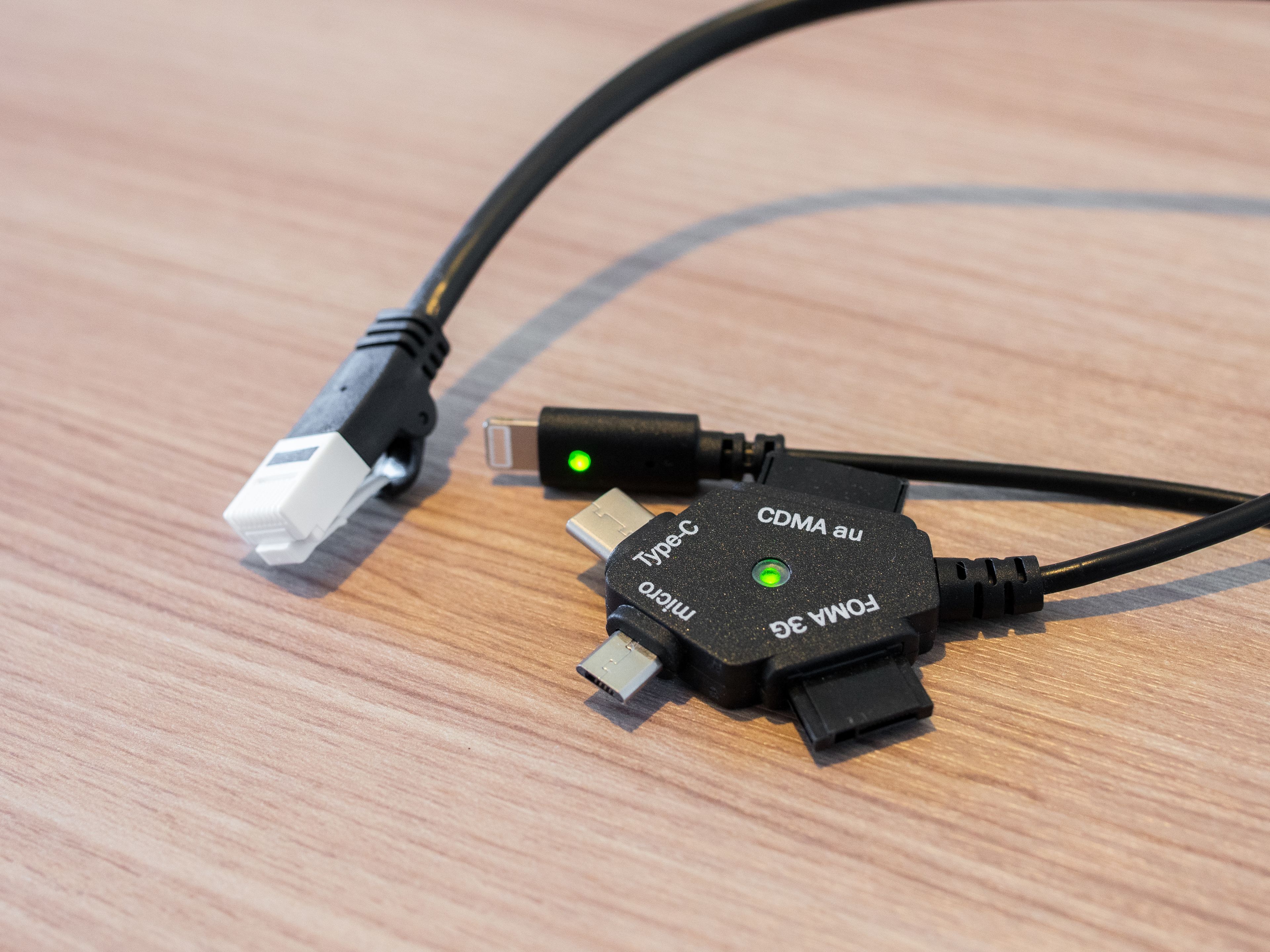 Un câble USB-C doté d’un connecteur de type C et d’un connecteur micro-USB, tous deux équipés de LED vertes, est posé sur une surface en bois.