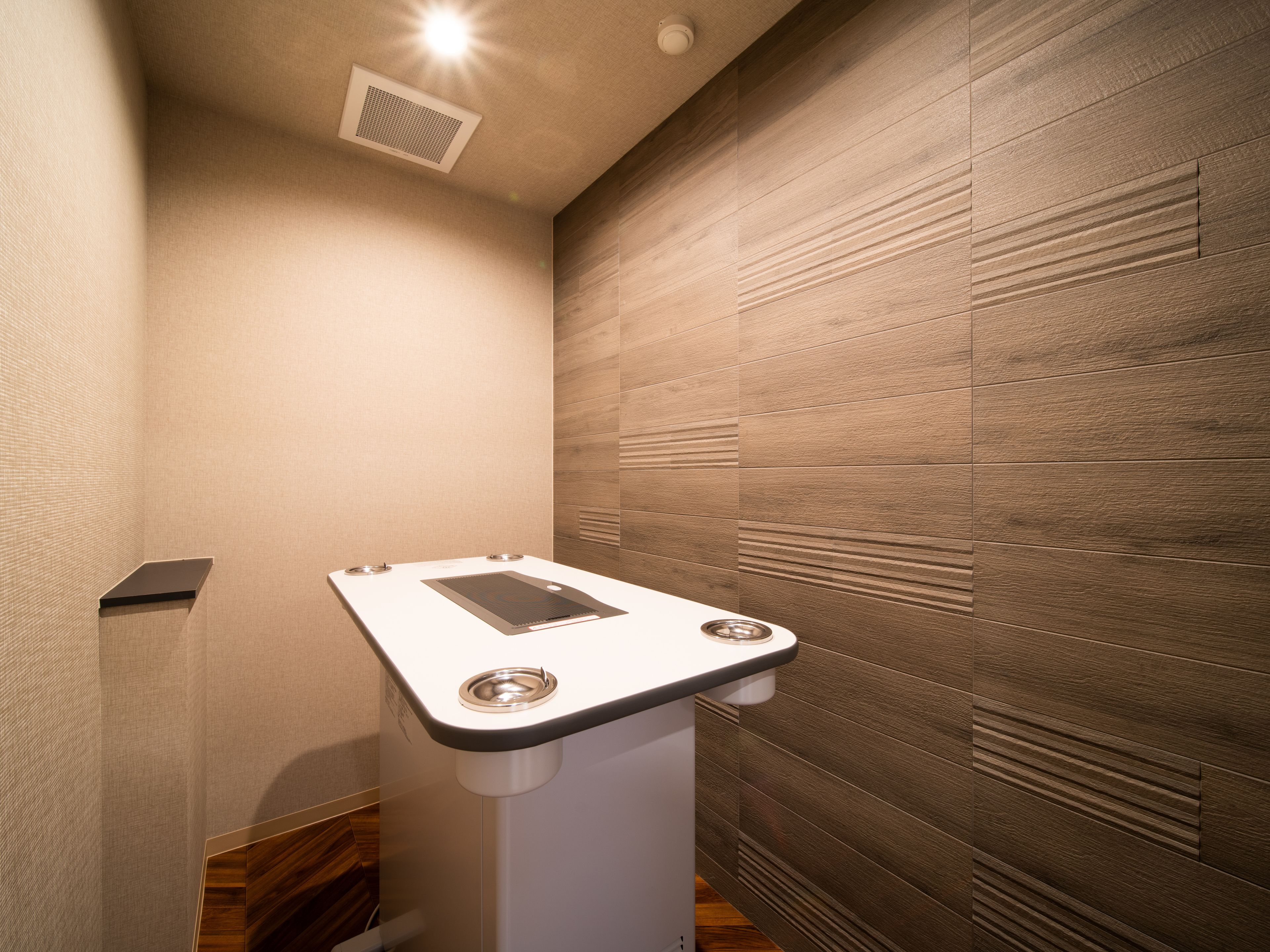 A modern bathroom with a wooden panel wall, a white pedestal sink, and a ceiling vent.