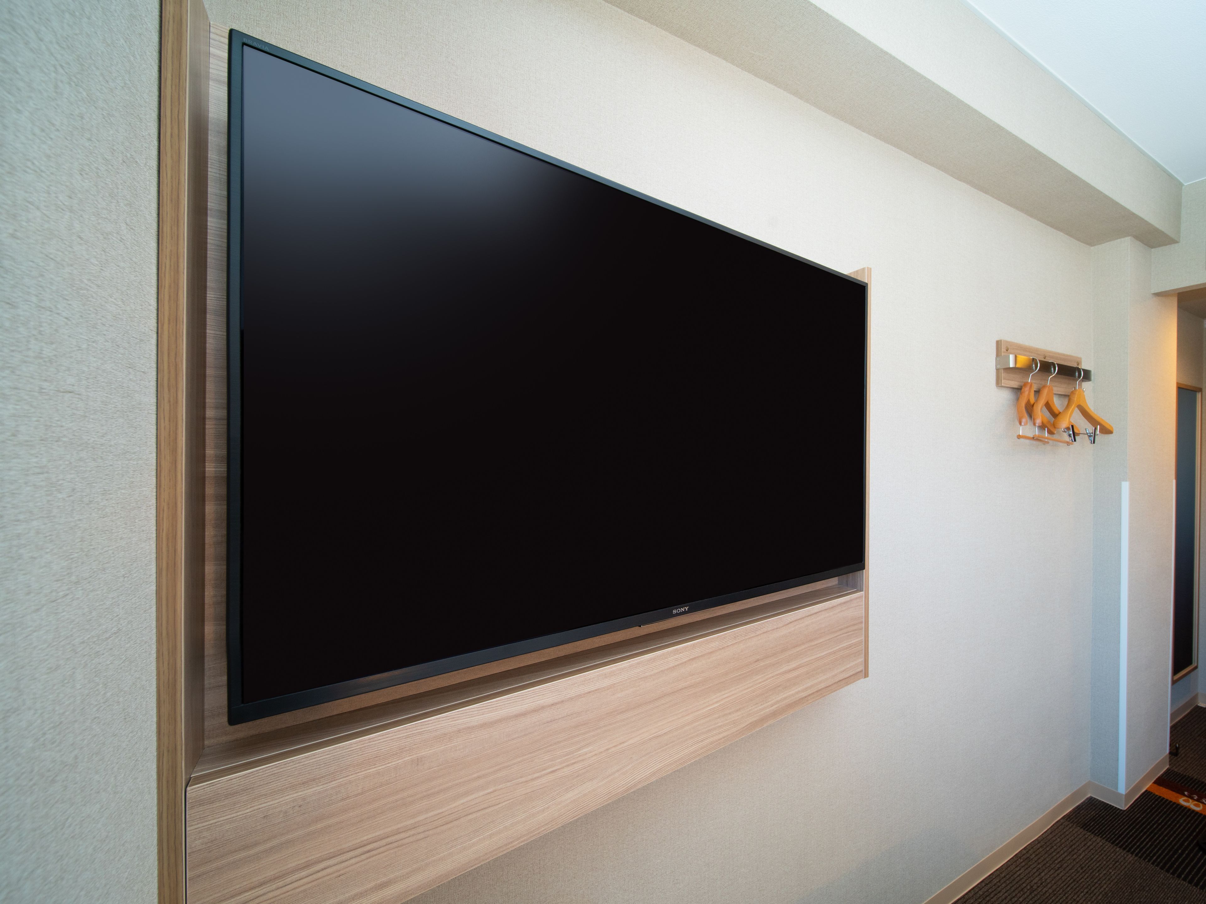 A large flat-screen TV mounted on a wall with a wooden panel below.