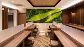 A modern bar area with wooden counters and stools, a green wall with a nature-inspired design, and a ceiling with recessed lighting. - Super Hotel Nagano Iida Inter (Iida)