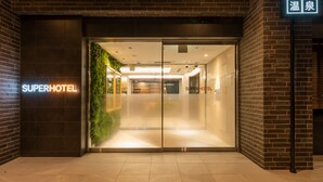 A hotel entrance with a modern design, featuring a glass door, a neon sign, and a brick facade. - Super Hotel Nagano Iida Inter (Iida)
