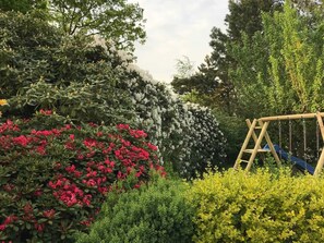 Un jardin avec une balançoire en bois, un feuillage dense et des arbustes en fleurs.