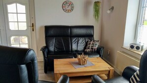 Een woonkamer met een zwarte leren bank, een houten salontafel en een kleine radio op een plank.