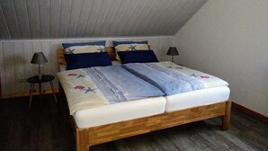 Een slaapkamer met een schuine kap, een houten bedframe, twee nachtkastjes met lampen en een bedsprei met dessin.
