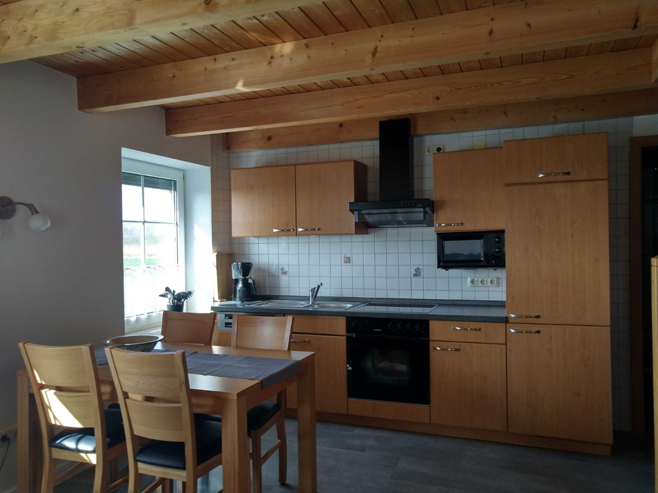 Une cuisine avec des meubles de rangement en bois, un micro-ondes noir, une cuisinière et une fenêtre.