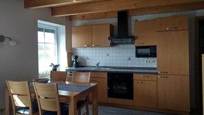 Een keuken met houten kastjes, een zwarte magnetron, een fornuis en een raam.