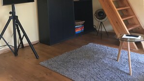 Ein Zimmer mit einem schwarzen Kleiderschrank, einer Holzleiter, einem Stativ mit einer Kamera und einem Flachbildfernseher.