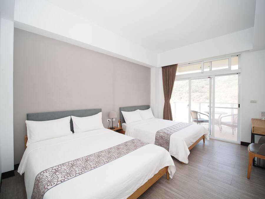 Une chambre d’hôtel avec deux lits, un balcon avec des chaises et un bureau.