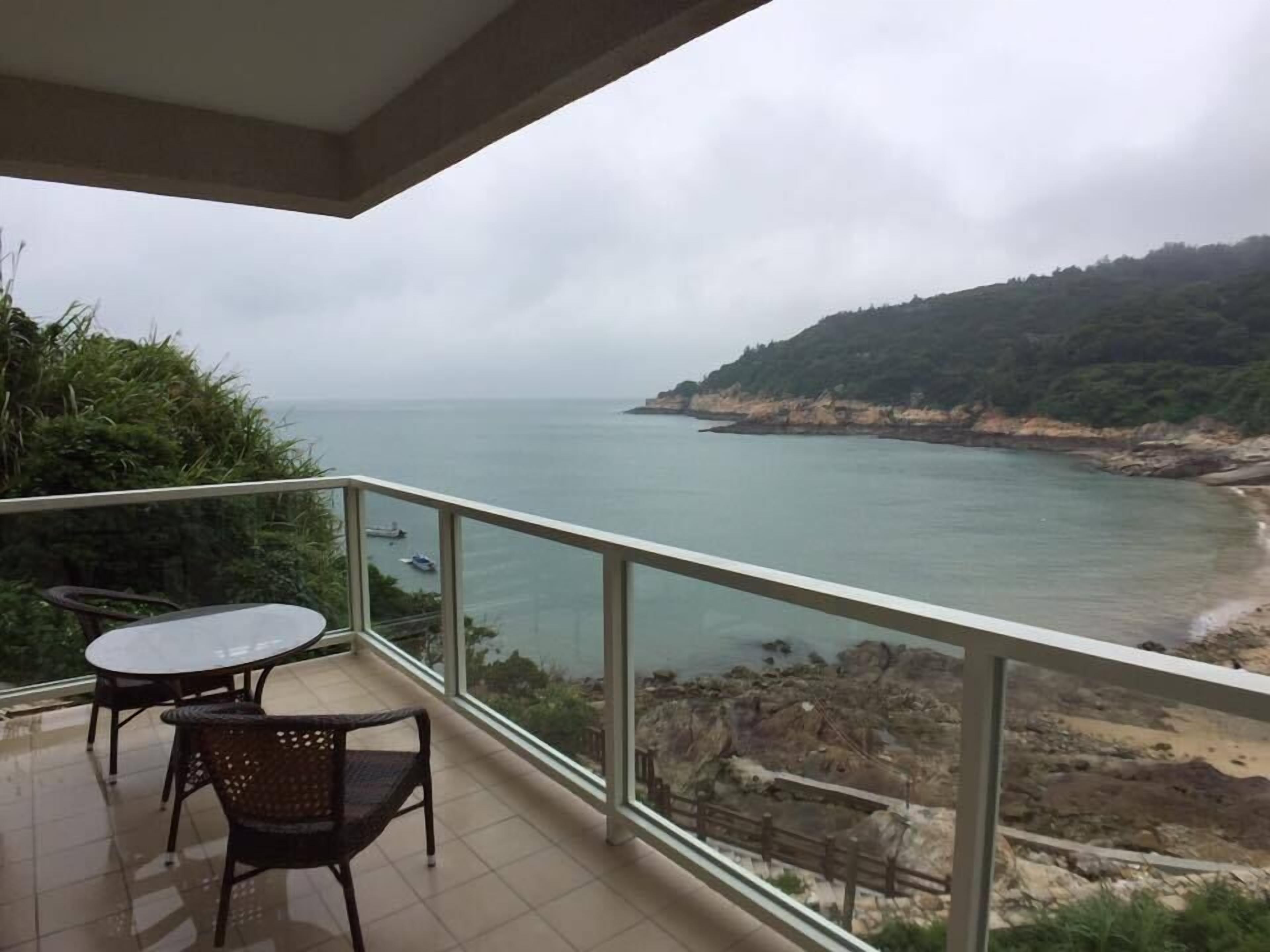 A balcony with a view of the sea, a table, and two chairs.