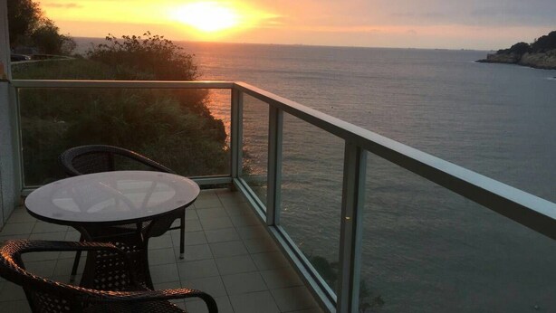 Un balcón con barandilla de cristal que ofrece vistas a la puesta de sol sobre el mar.