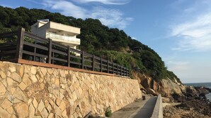 Edificio costero con pared de piedra, cerca de madera y balcón con vista al mar.