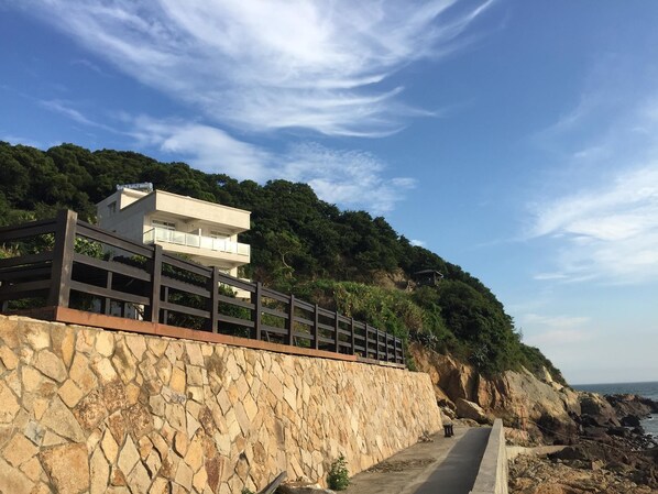 Edificio costero con pared de piedra, cerca de madera y balcón con vista al mar.