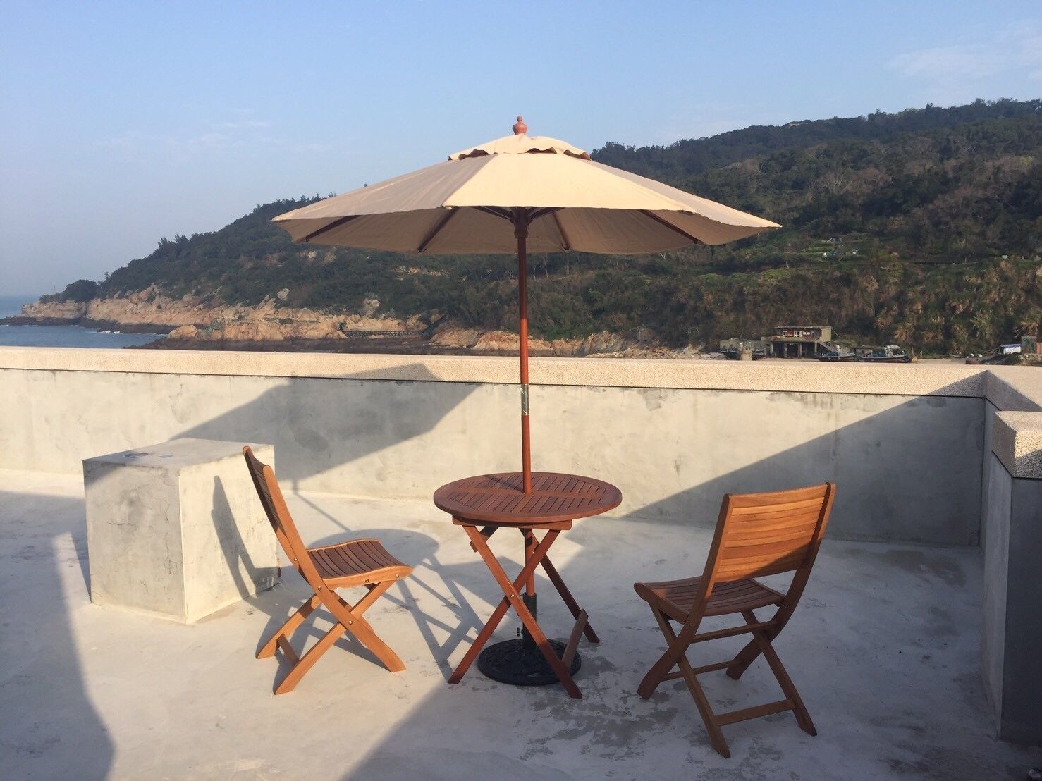 A terrace with a table and two chairs, an umbrella, and a view of the coastline.